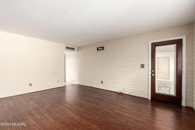 spare room with baseboards, brick wall, visible vents, and wood finished floors
