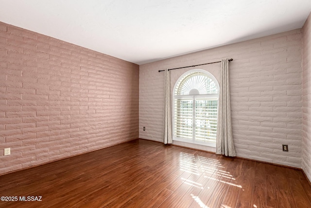 unfurnished room featuring brick wall and wood finished floors