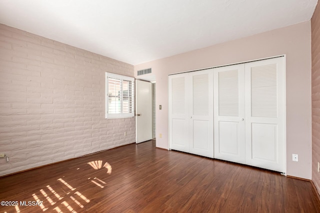 unfurnished bedroom featuring visible vents, wood finished floors, brick wall, and a closet