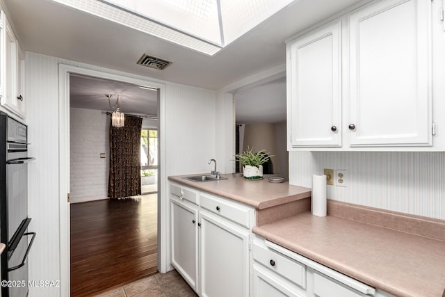 kitchen with a sink, light countertops, white cabinetry, and visible vents