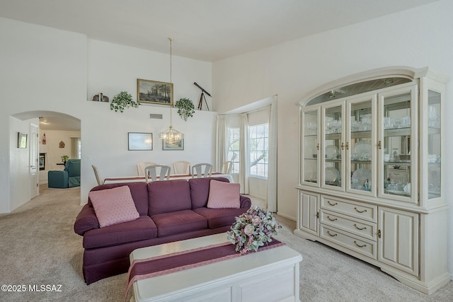 living area featuring arched walkways, baseboards, a towering ceiling, and light colored carpet