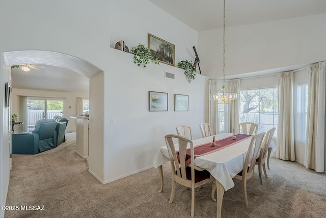dining area featuring visible vents, light colored carpet, arched walkways, an inviting chandelier, and a high ceiling