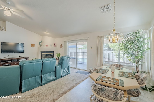 living room featuring visible vents, a glass covered fireplace, ceiling fan with notable chandelier, and vaulted ceiling