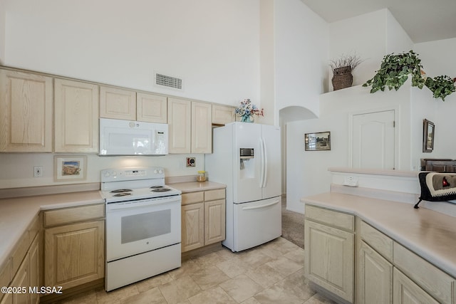 kitchen featuring light brown cabinets, white appliances, light countertops, a towering ceiling, and visible vents
