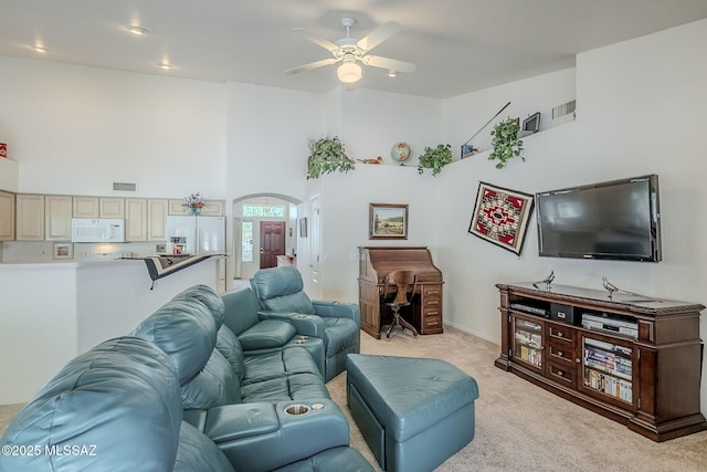 living room with ceiling fan, light colored carpet, arched walkways, a towering ceiling, and visible vents