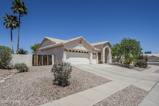ranch-style house featuring fence, an attached garage, a tile roof, stucco siding, and concrete driveway