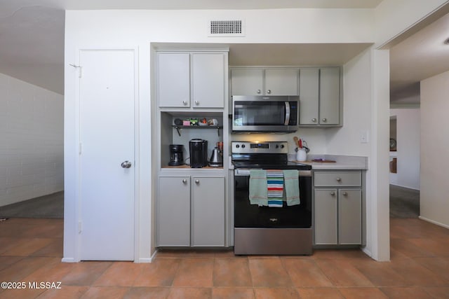 kitchen with light countertops, gray cabinets, stainless steel appliances, light tile patterned floors, and visible vents