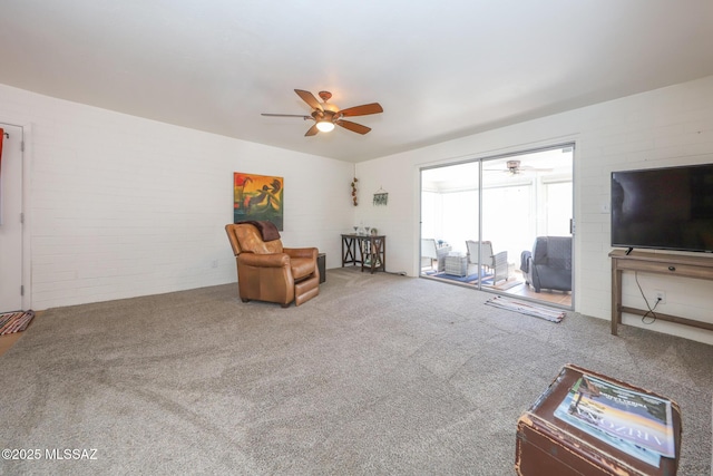 living area with carpet floors, a ceiling fan, and brick wall