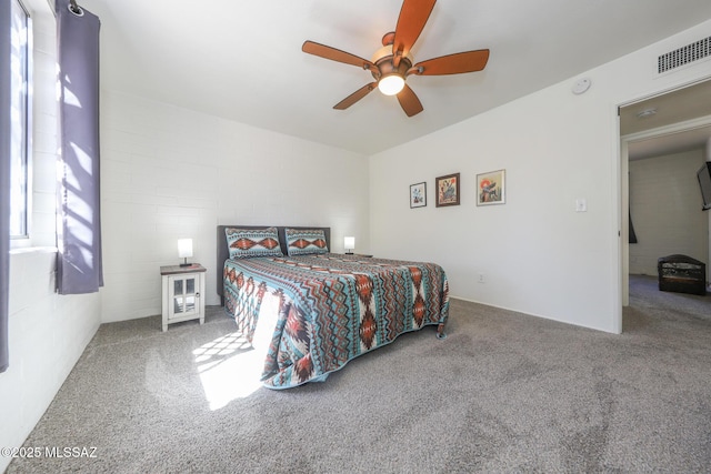 carpeted bedroom with visible vents, ceiling fan, and concrete block wall