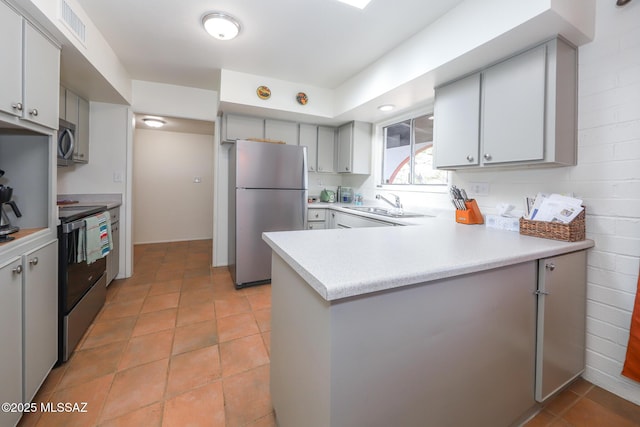 kitchen with appliances with stainless steel finishes, a sink, light countertops, a peninsula, and visible vents