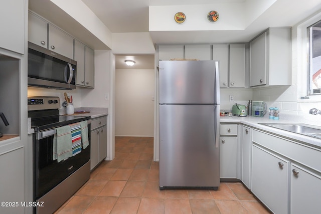 kitchen with appliances with stainless steel finishes, a sink, light countertops, gray cabinets, and light tile patterned floors