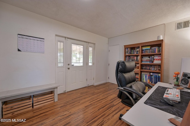 office area featuring a textured ceiling, wood finished floors, visible vents, and baseboards