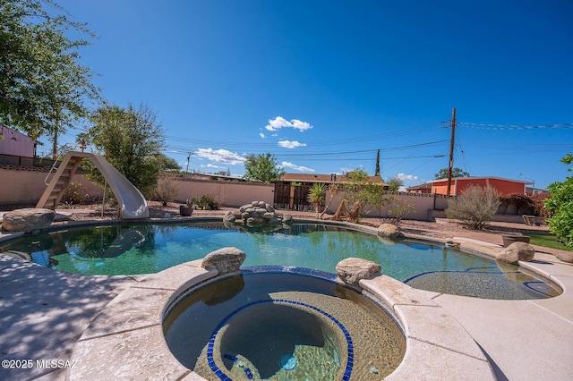view of pool featuring a pool with connected hot tub, a water slide, and a fenced backyard