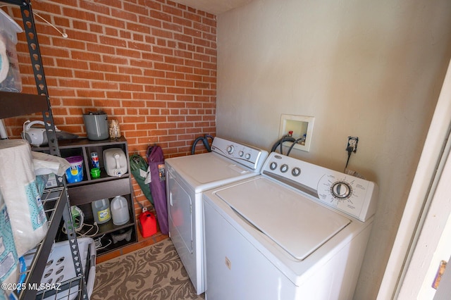 clothes washing area with brick wall, washer and clothes dryer, and laundry area
