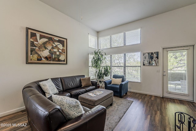 living area featuring baseboards, dark wood finished floors, a towering ceiling, and a healthy amount of sunlight