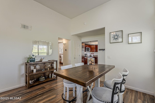 dining area featuring visible vents, baseboards, dark wood-type flooring, and a towering ceiling