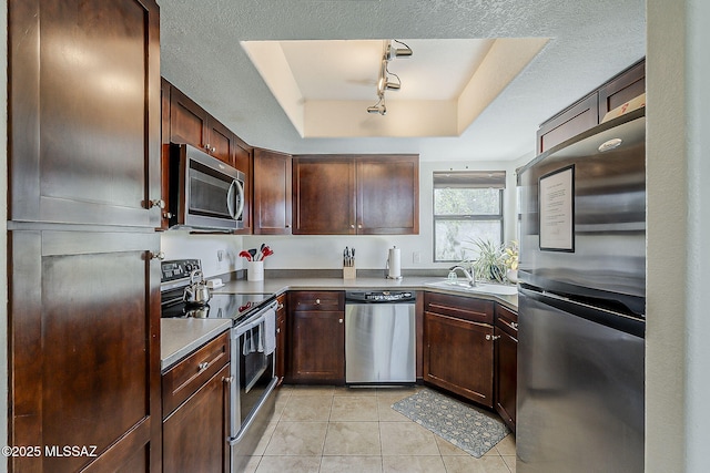 kitchen featuring track lighting, a raised ceiling, a sink, light tile patterned floors, and stainless steel appliances