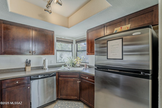 kitchen with dark brown cabinetry, appliances with stainless steel finishes, a sink, light tile patterned floors, and track lighting