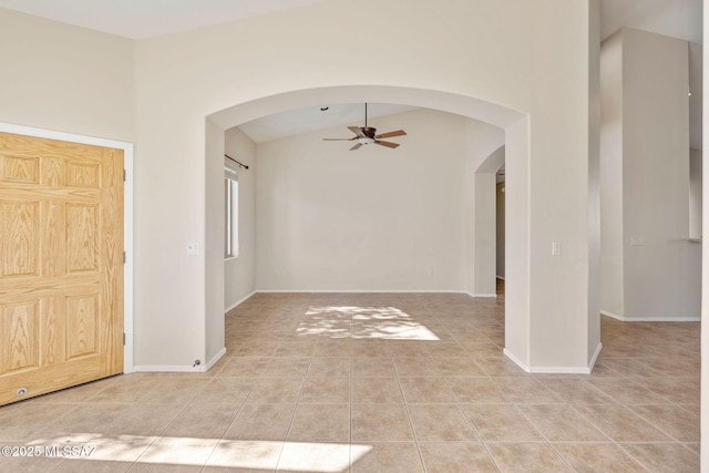 empty room featuring arched walkways, ceiling fan, light tile patterned flooring, and vaulted ceiling