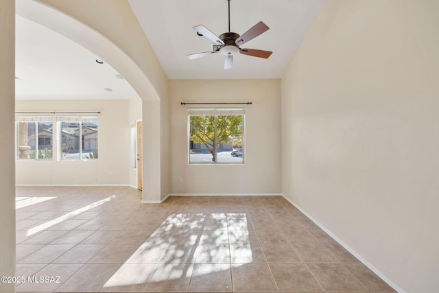 tiled empty room featuring arched walkways, baseboards, a ceiling fan, and vaulted ceiling