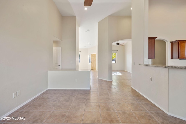 interior space featuring light tile patterned flooring, ceiling fan, arched walkways, and a towering ceiling