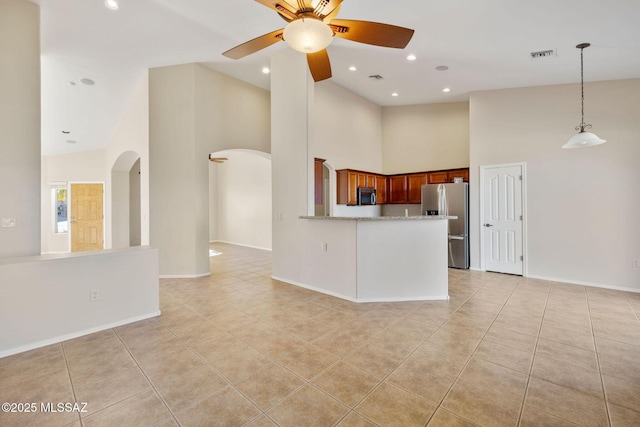 unfurnished living room featuring ceiling fan, arched walkways, light tile patterned floors, a towering ceiling, and visible vents