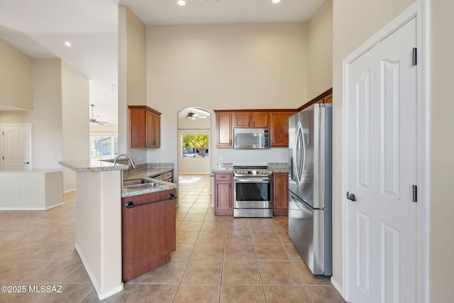 kitchen featuring a ceiling fan, appliances with stainless steel finishes, a sink, light tile patterned floors, and a peninsula