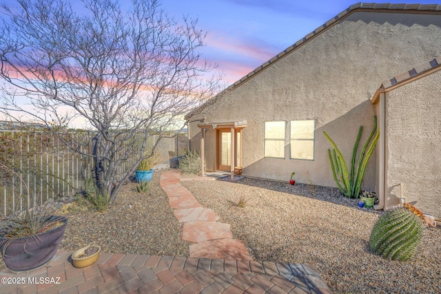 back of house at dusk with stucco siding and fence