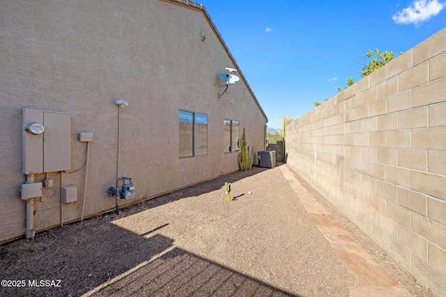 view of side of home with fence, central AC unit, and stucco siding
