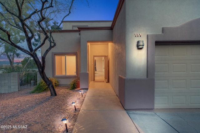 view of exterior entry featuring stucco siding and fence