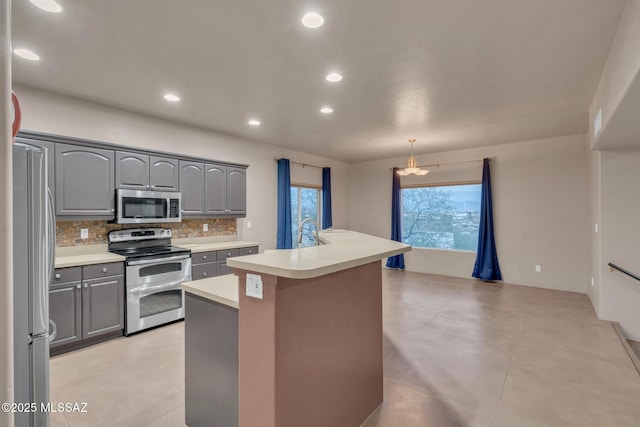 kitchen with decorative backsplash, a kitchen island with sink, appliances with stainless steel finishes, gray cabinetry, and light countertops