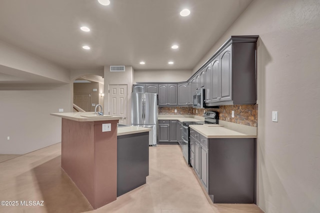 kitchen featuring gray cabinets, visible vents, arched walkways, stainless steel appliances, and an island with sink