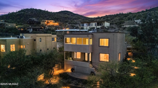 back of property at dusk with a mountain view and stucco siding