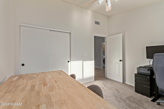 unfurnished office with ceiling fan, visible vents, carpet, and a towering ceiling