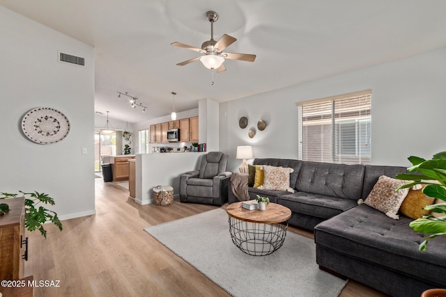 living room featuring visible vents, baseboards, ceiling fan, light wood-style flooring, and vaulted ceiling