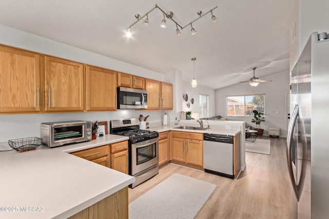 kitchen with appliances with stainless steel finishes, light wood-type flooring, a toaster, a sink, and a peninsula