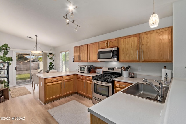 kitchen with vaulted ceiling, a sink, a peninsula, stainless steel appliances, and light wood-style flooring