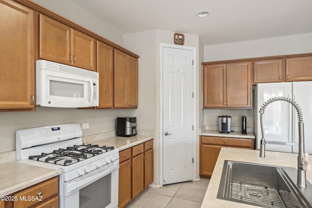 kitchen with light countertops, a sink, brown cabinetry, and white appliances