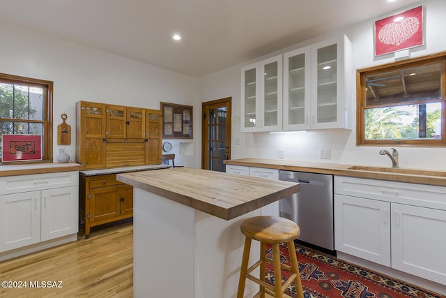 kitchen featuring white cabinets, butcher block counters, a sink, stainless steel dishwasher, and glass insert cabinets