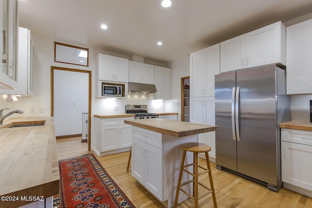 kitchen with a sink, butcher block countertops, stainless steel appliances, white cabinetry, and under cabinet range hood