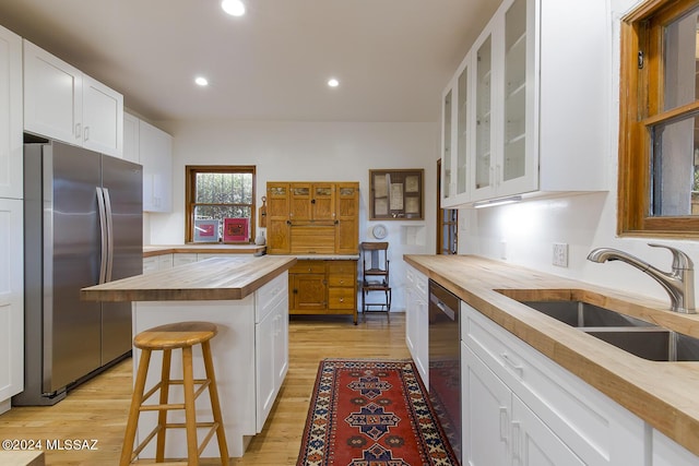 kitchen with a sink, light wood finished floors, butcher block countertops, stainless steel appliances, and glass insert cabinets