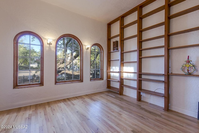 empty room featuring baseboards, a textured wall, and light wood finished floors