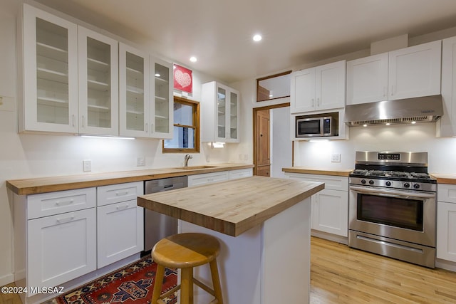 kitchen featuring white cabinets, appliances with stainless steel finishes, a sink, under cabinet range hood, and butcher block counters