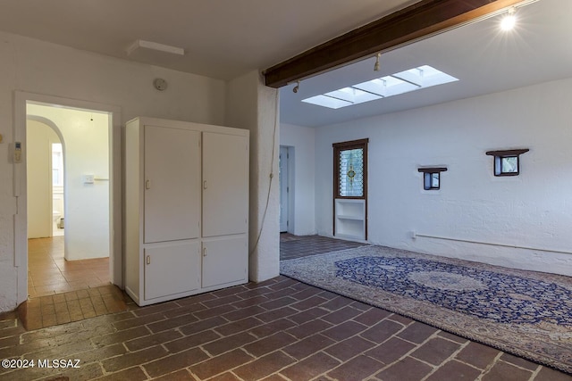 entryway featuring arched walkways, brick floor, a skylight, and beamed ceiling