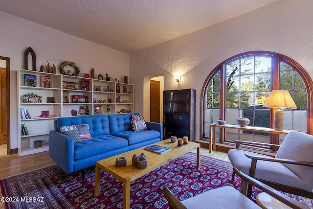 living area featuring arched walkways, a textured wall, and wood finished floors