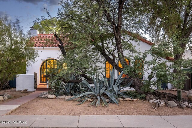mediterranean / spanish home featuring a tiled roof, a chimney, and stucco siding