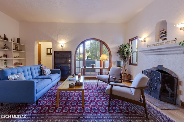 living area featuring arched walkways, a textured wall, wood finished floors, and a fireplace
