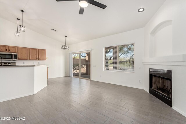 unfurnished living room featuring a fireplace, a ceiling fan, visible vents, vaulted ceiling, and wood finished floors