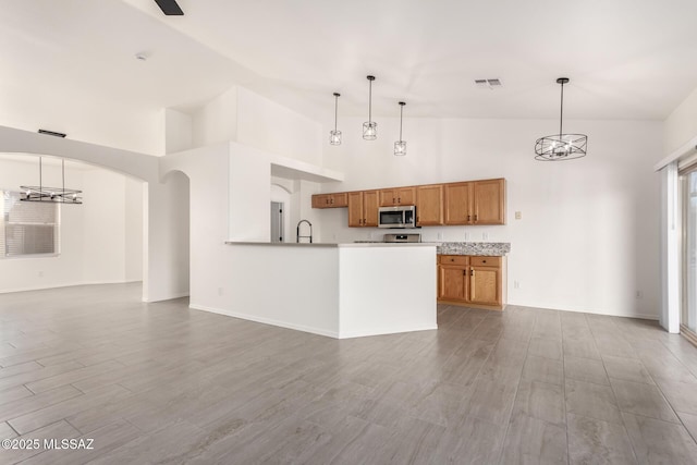 kitchen featuring stainless steel microwave, a sink, high vaulted ceiling, brown cabinetry, and visible vents