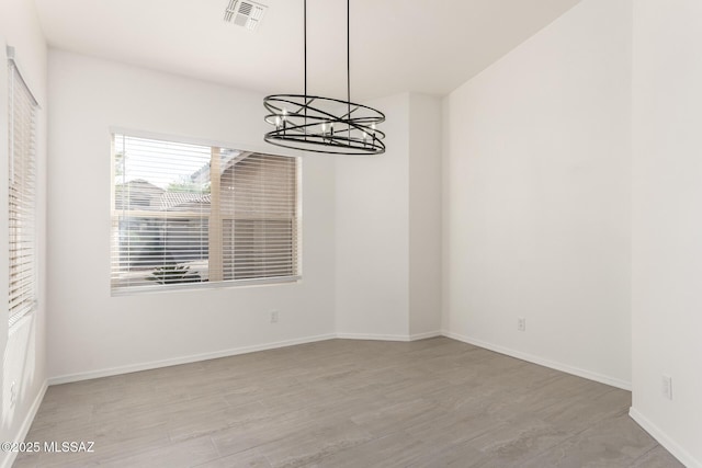 unfurnished dining area featuring an inviting chandelier, visible vents, wood finished floors, and baseboards
